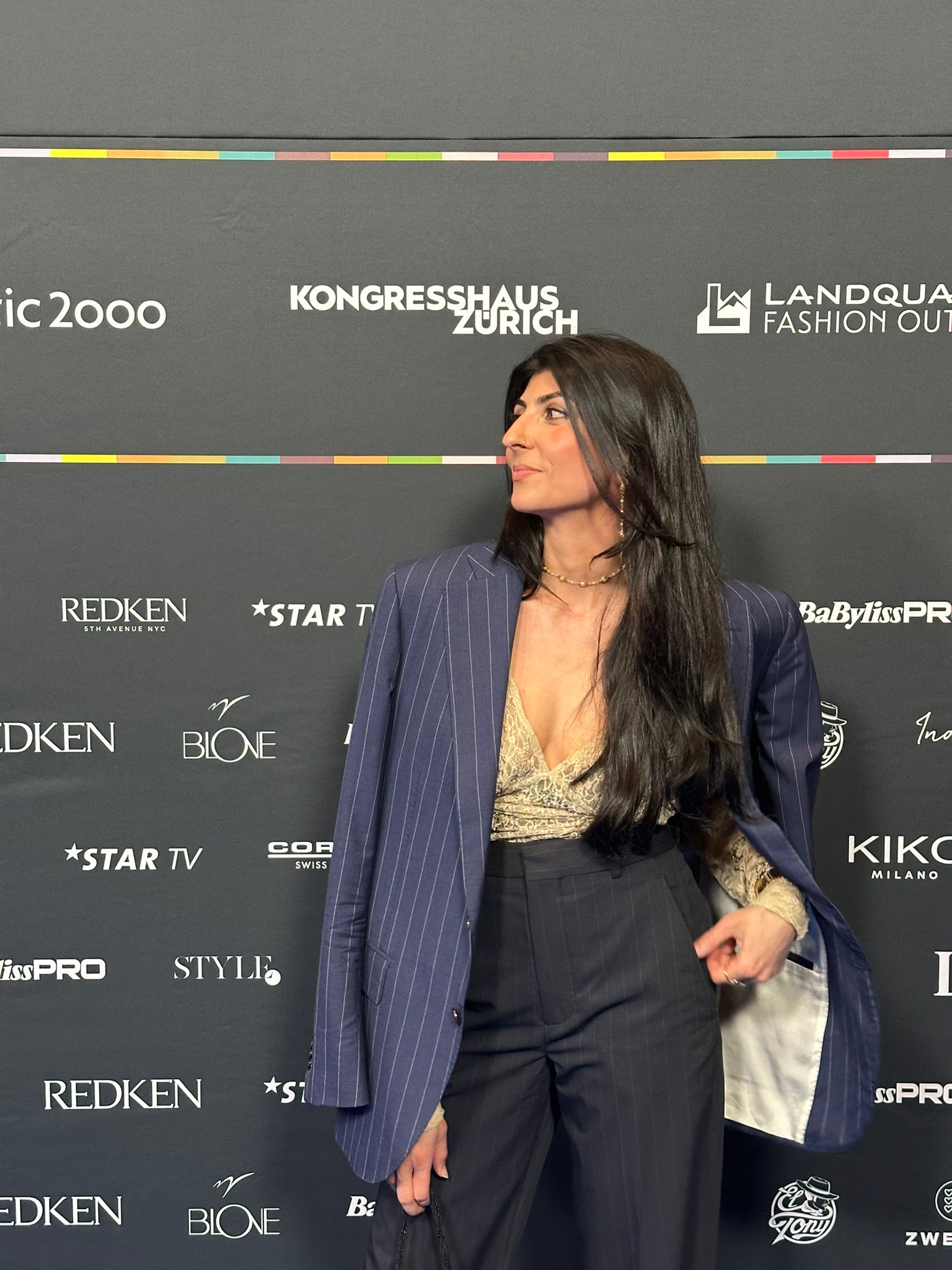 Junge Frau mit schwarzen langen Haaren vor einer Fotowand seitlich posierend trägt einen Marine blauen Oversized Blazer