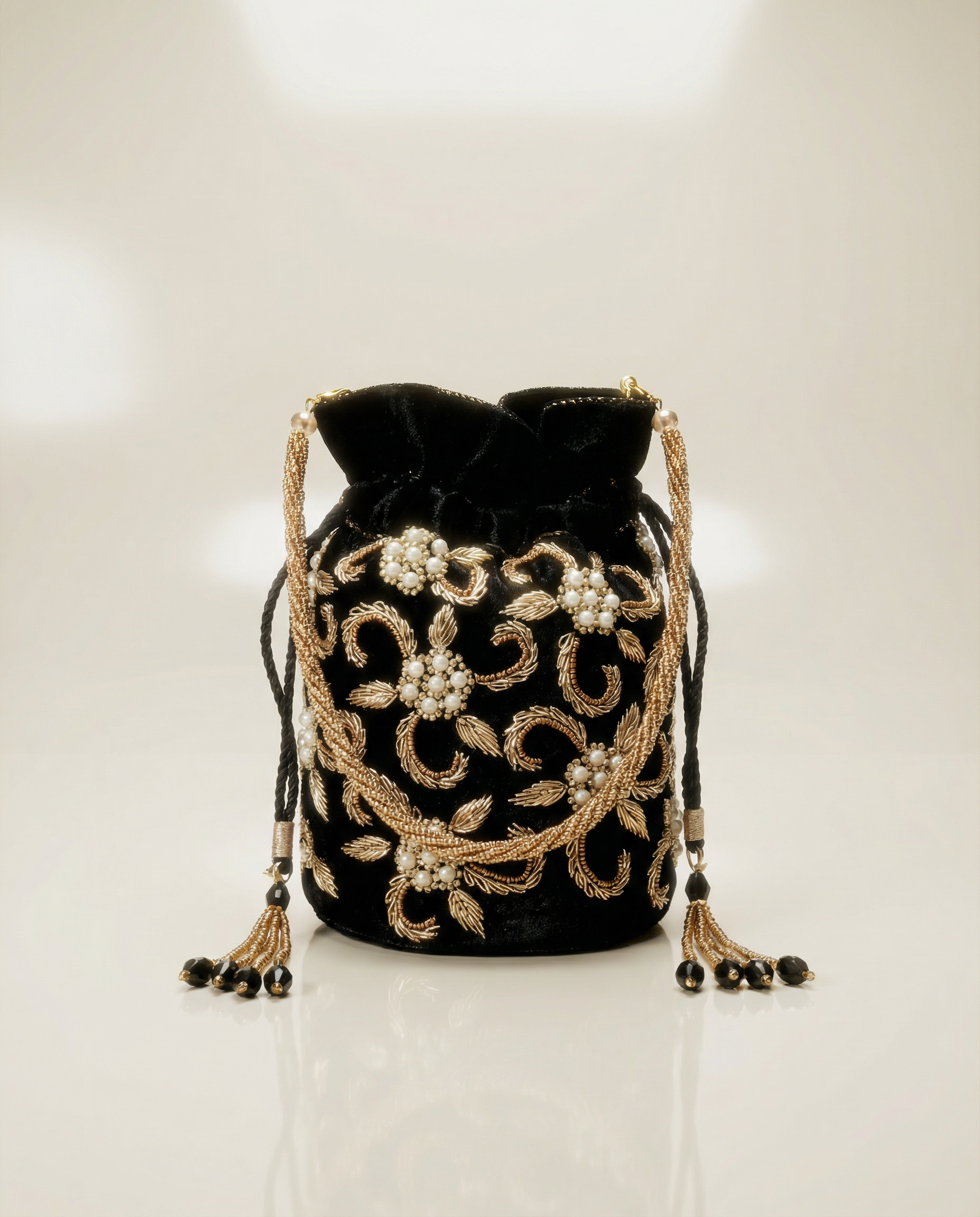 Schwarze Potli Bag aus Samt mit goldener Stickerei und Perlenverzierung auf glänzendem Hintergrund