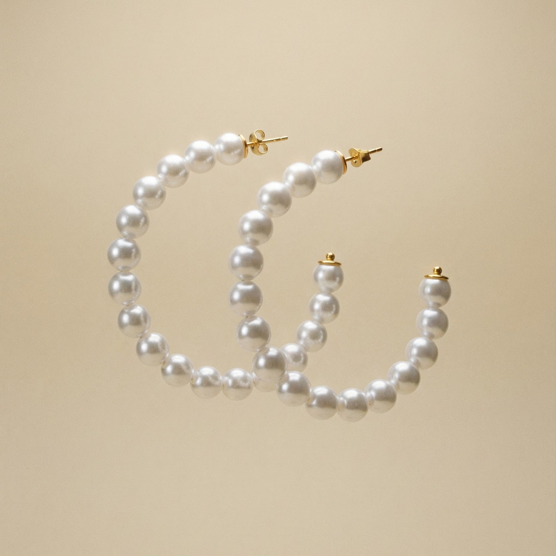 Creolen mit Süsswasserperlen bestezt auf beigem Hintergrund.