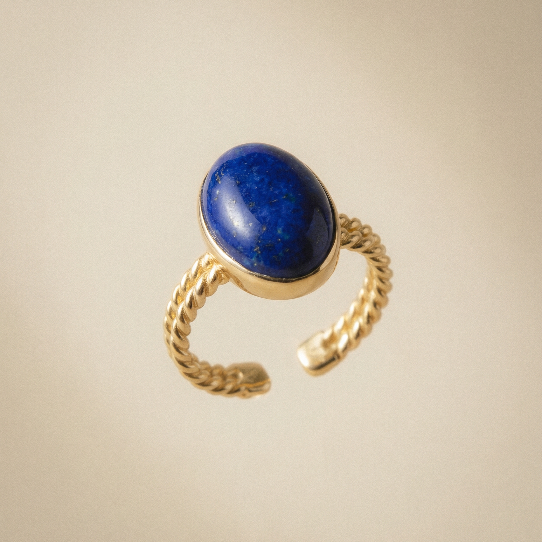 Goldener Ring mit Lapislazuli besetztem Stein auf beigem Hintergrund.