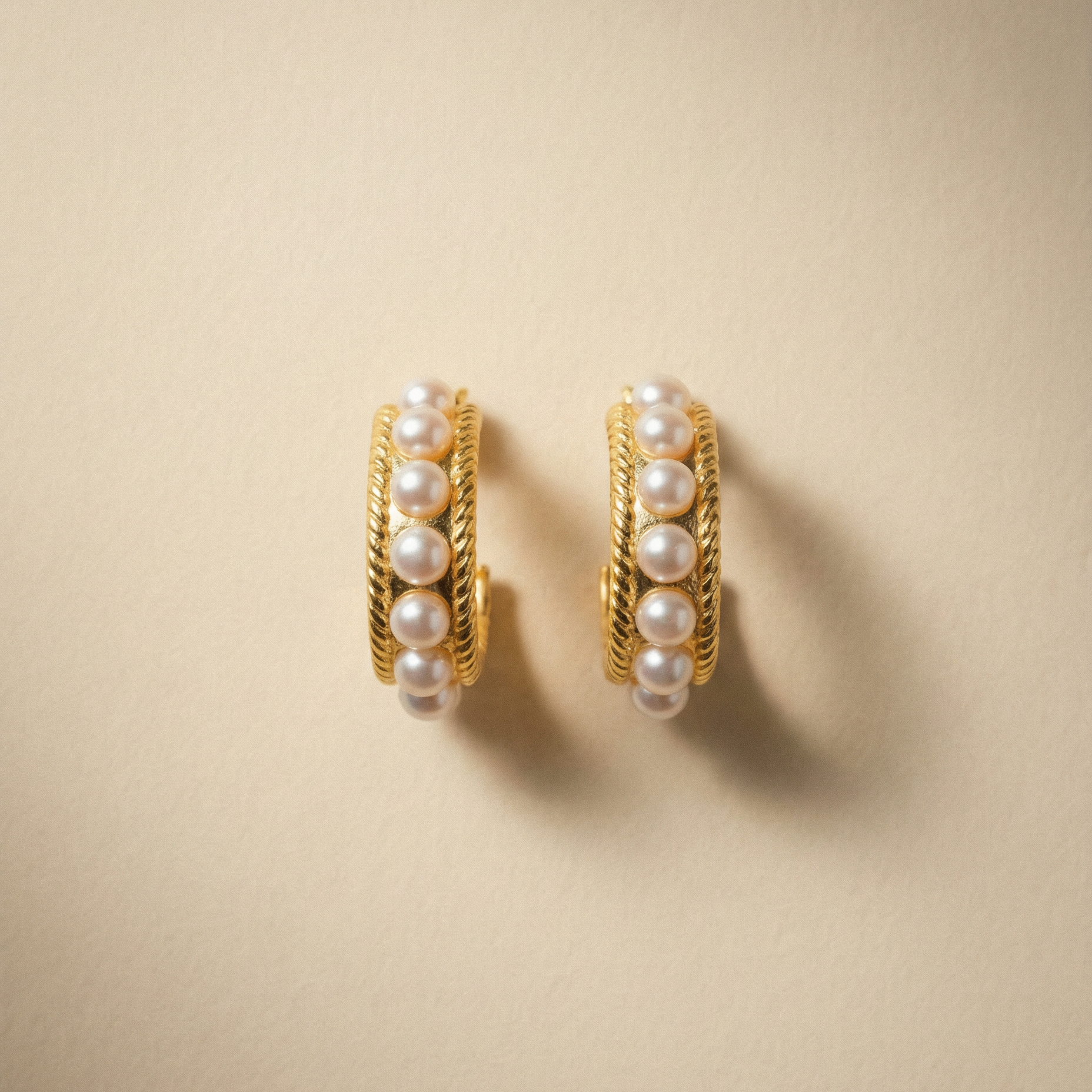 Goldene Creolen mit Süsswasserperlen besetzt auf beigem Hintergrund