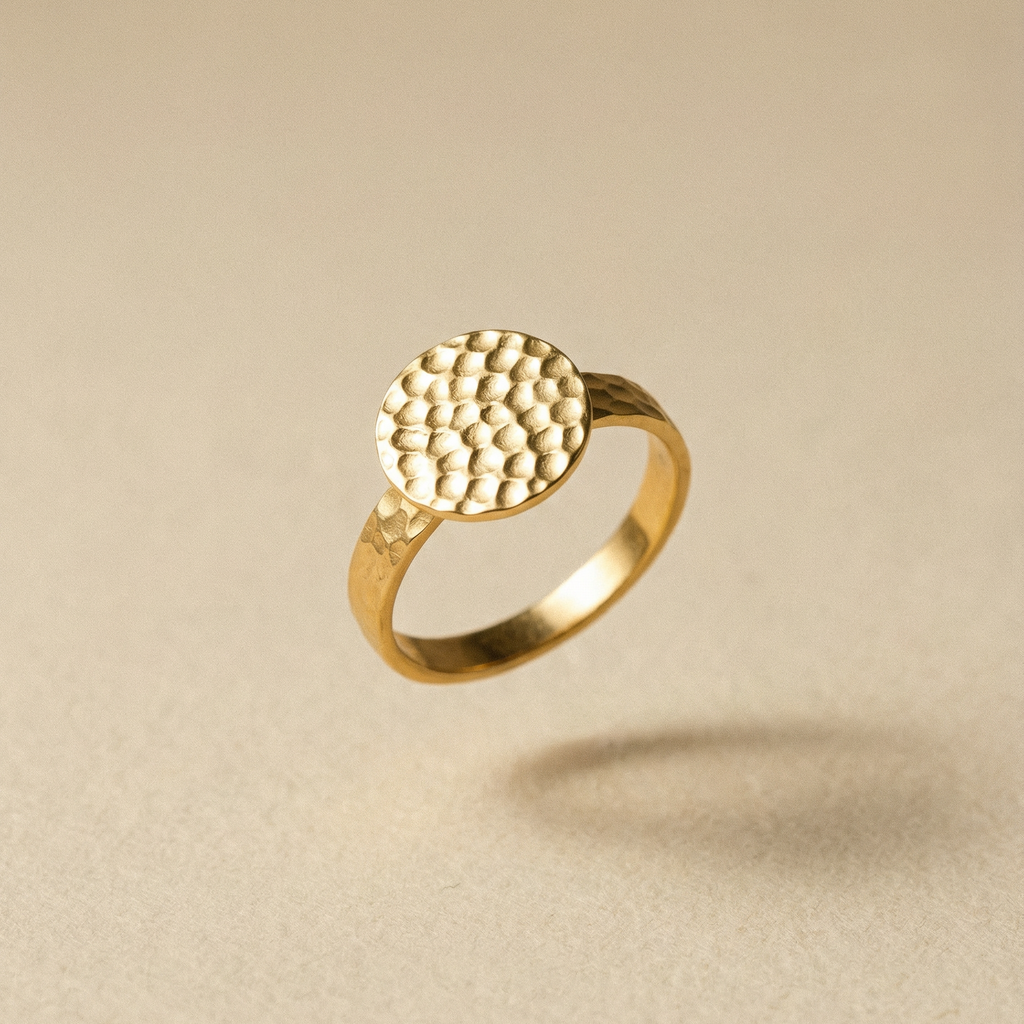 Goldener Ring mit handgehämmerter Textur auf dem Siegel auf beigem Hintergrund