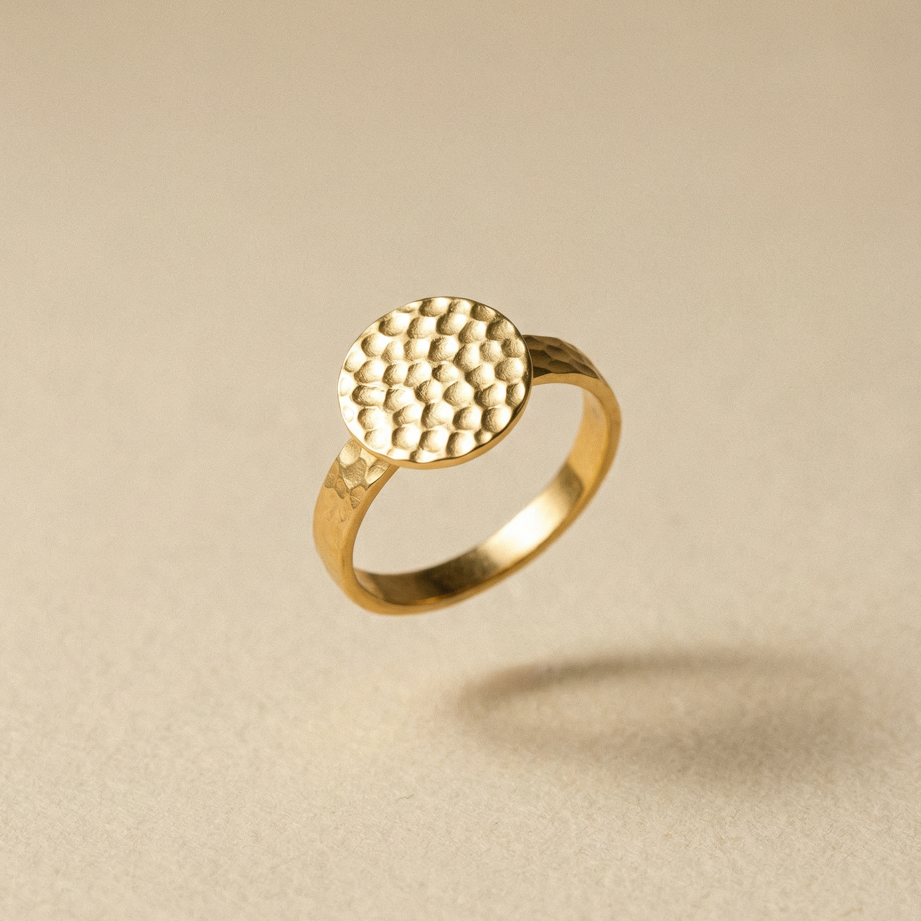 Goldener Ring mit handgehämmerter Textur auf dem Siegel auf beigem Hintergrund