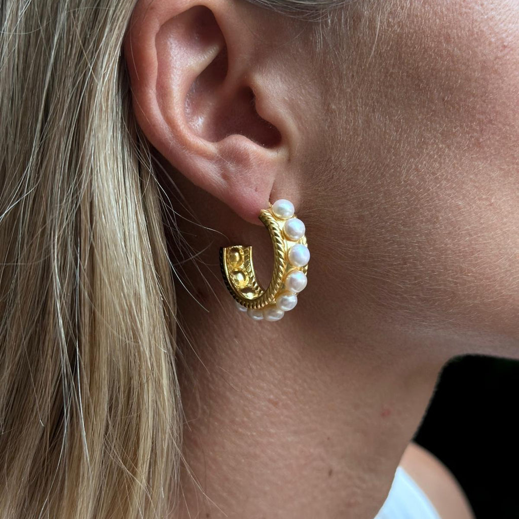 Close Up eines Ohrrings. Goldene Creolen mit Süsswasserperlenbesetzt an einem Ohr