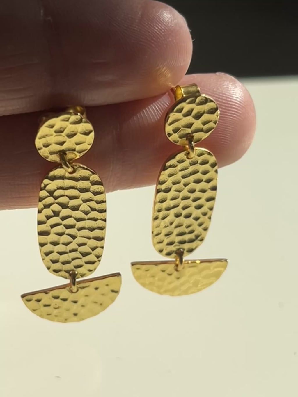handgehämmerte vergoldete Ohrringe auf beigem Hintergrund